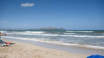 A beach with clear skies, waves, and distant mountains.