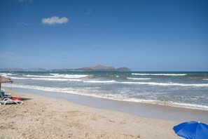 Una playa con cielos despejados, olas y montañas a lo lejos.
