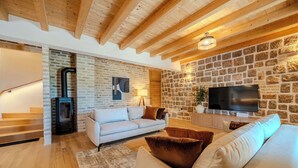 Ein Wohnzimmer mit Steinwand, Kamin, einer Couch, einem Fernseher und Holzbalken an der Decke.