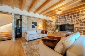 Ein Wohnzimmer mit Steinwand, Kamin, einer Couch, einem Fernseher und Holzbalken an der Decke.