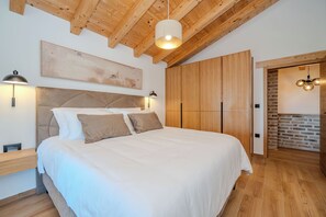 Une chambre à coucher avec un grand lit, des poutres apparentes en bois au plafond, une tête de lit, des lampes de chevet et une armoire.