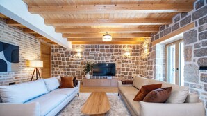 Ein modernes Wohnzimmer mit einer Steinsäule, Holzbalken an der Decke, einem Flachbildfernseher und zwei Sofas.