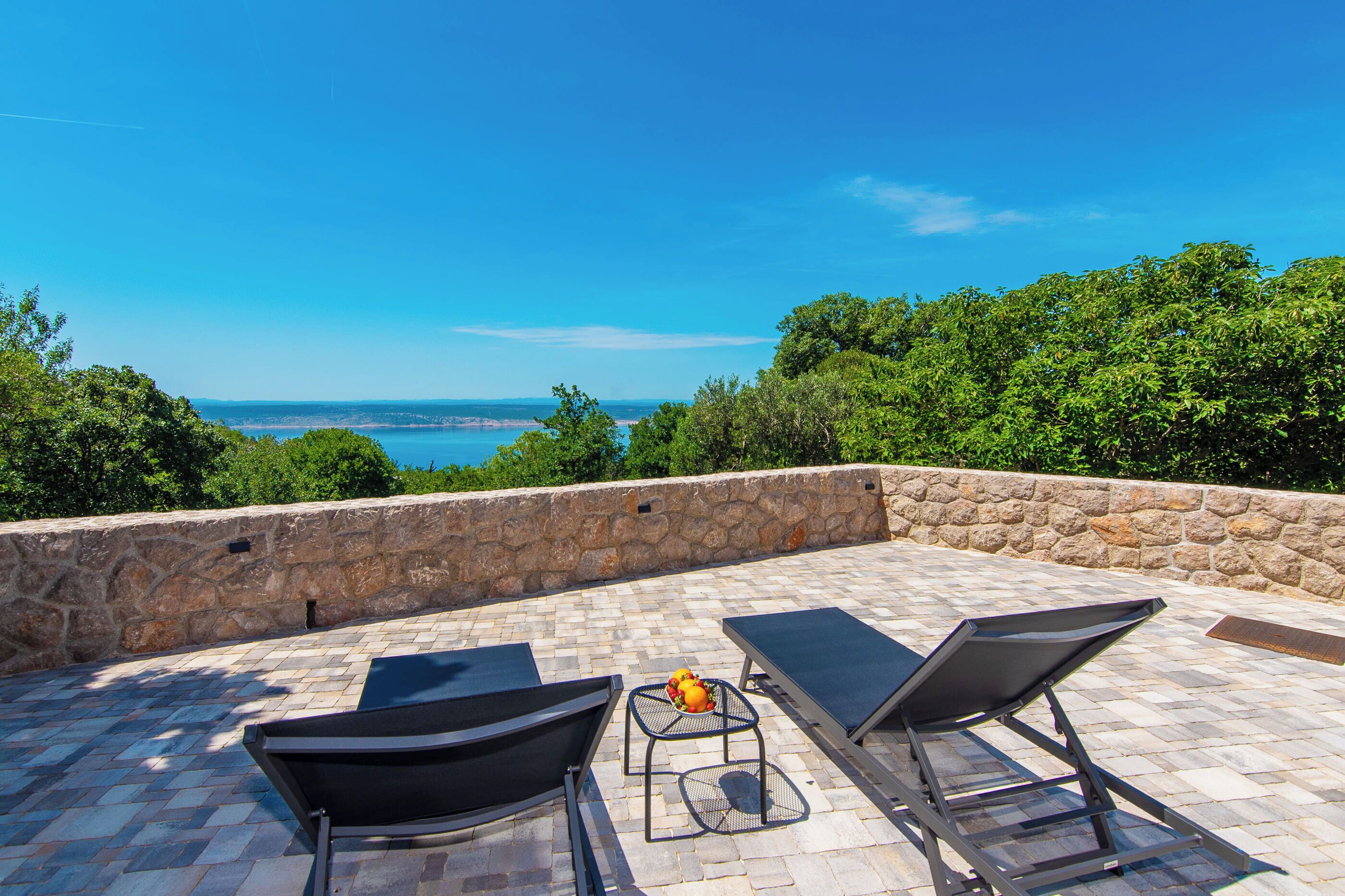 A rooftop terrace with two lounge chairs, a small table, and a view of the sea.