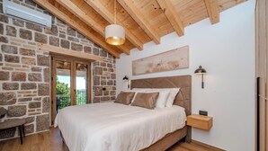Ein Schlafzimmer mit Steinsandsteinwand, Holzbalkendecke, einem Bett, Nachttischlampen und Blick durch eine Tür.