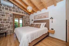 Ein Schlafzimmer mit Steinsandsteinwand, Holzbalkendecke, einem Bett, Nachttischlampen und Blick durch eine Tür.