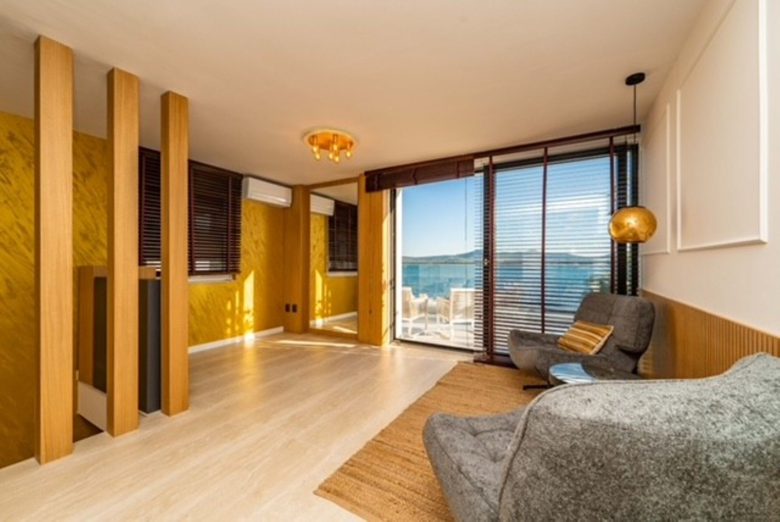 A modern living room with a sofa, a rug, and a view through large windows.