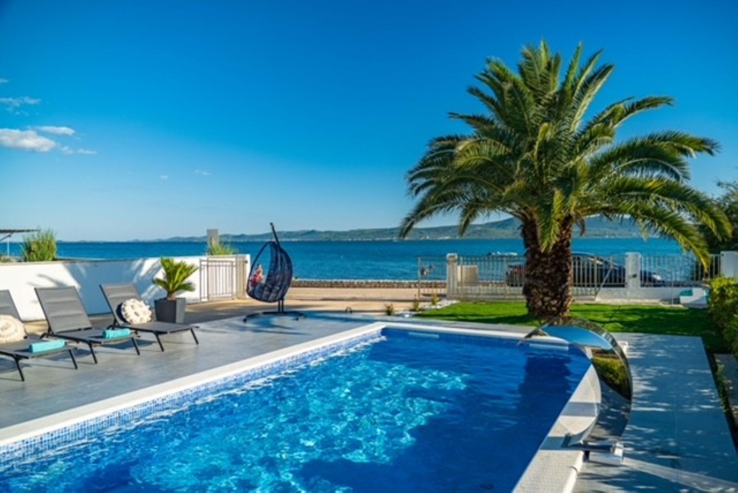 A swimming pool with lounge chairs and a palm tree, overlooking a body of water.