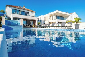 A modern poolside area with lounge chairs, a clear blue pool, and contemporary buildings in the background. - Villa Morea (Sukosan)