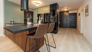 Een moderne keuken met een centraal eiland, barstoelen, een inbouwoven en een koelkast.