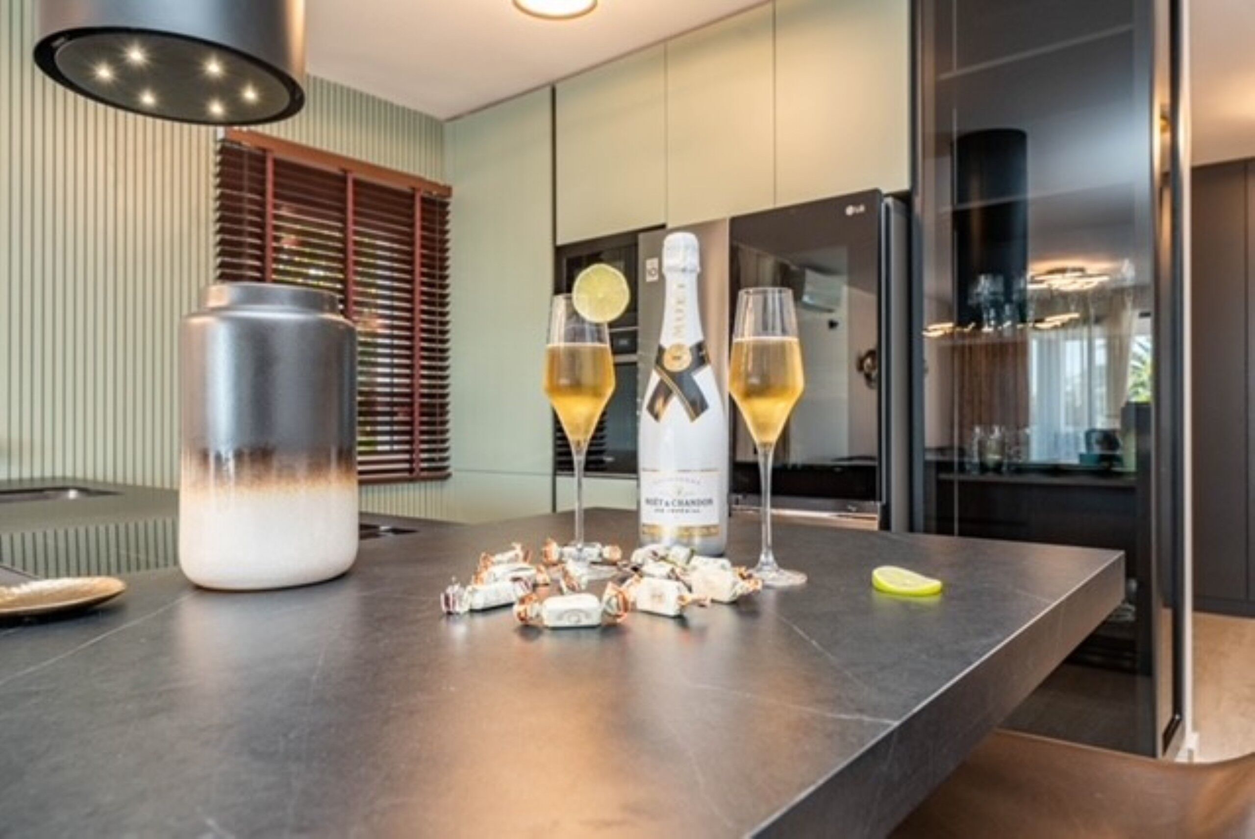 Une cuisine moderne avec un îlot central en acier inoxydable, une bouteille de champagne, deux verres et une bouteille de champagne décorative.
