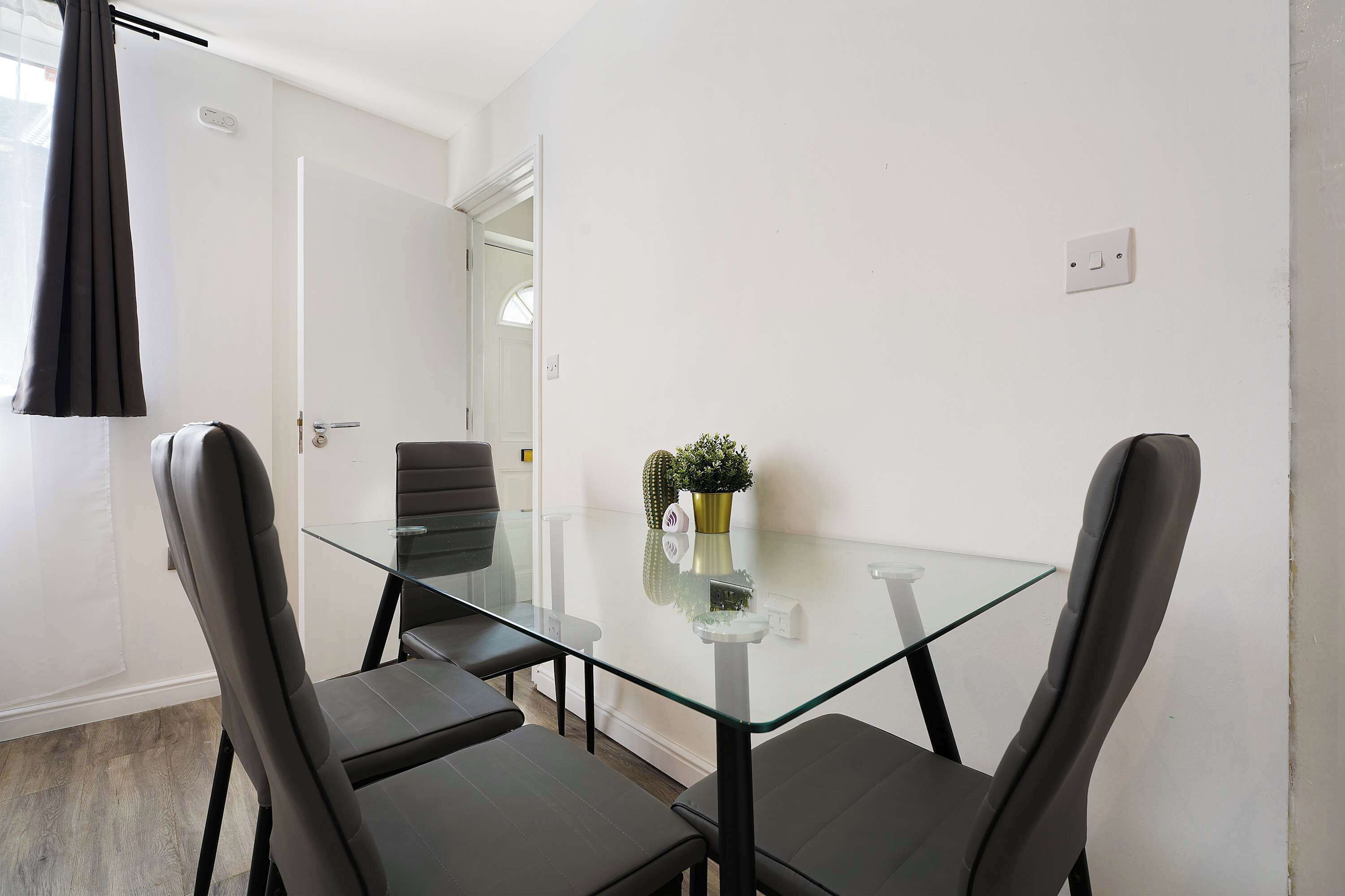 A small, modern room with a glass table and two chairs, a door, and a window with curtains.