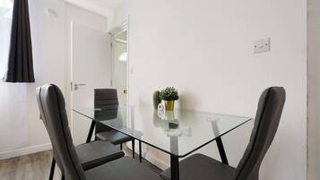 A small, modern room with a glass table and two chairs, a door, and a window with curtains.