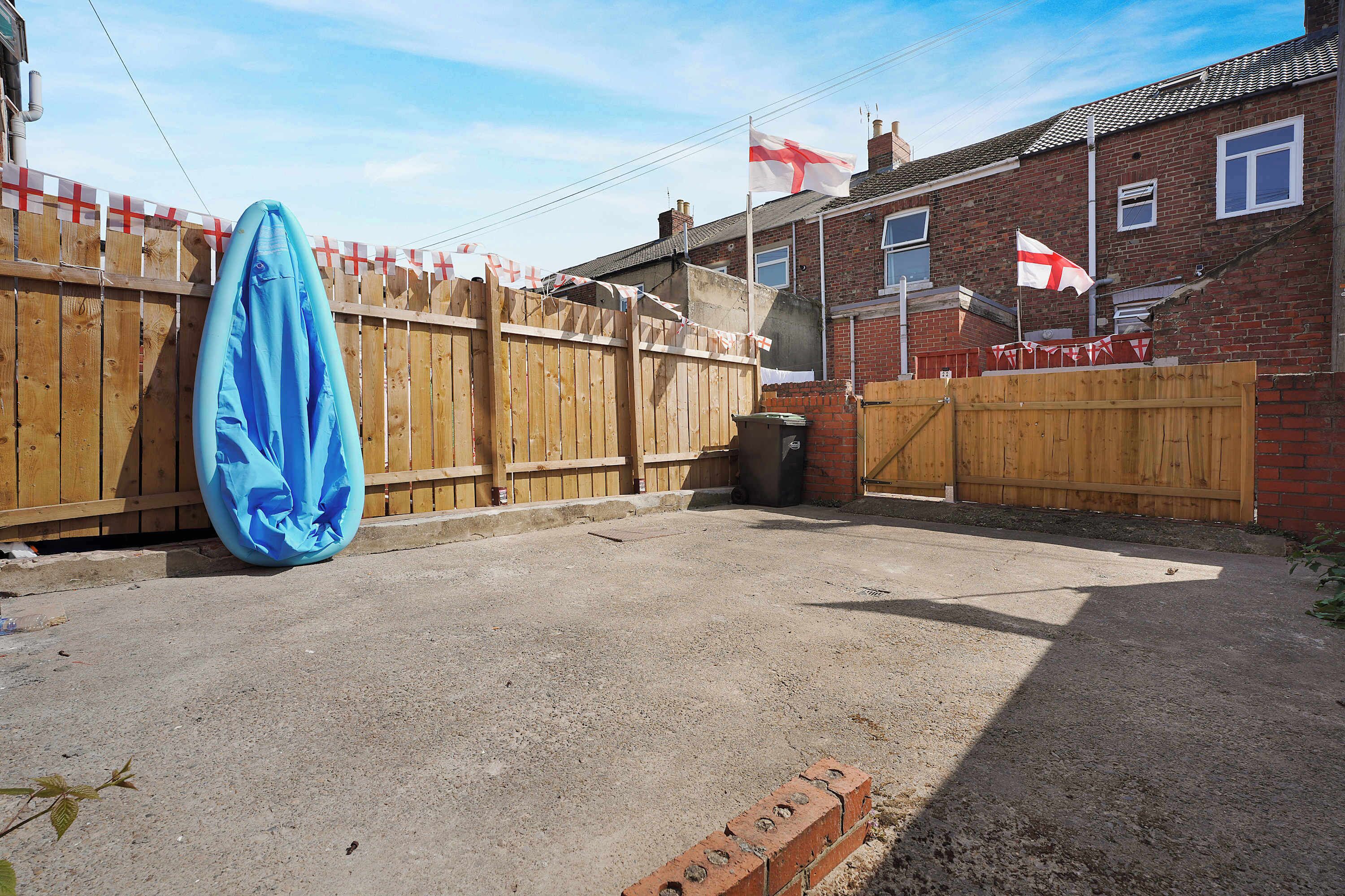 A backyard with a wooden fence, a blue object, and a brick wall.