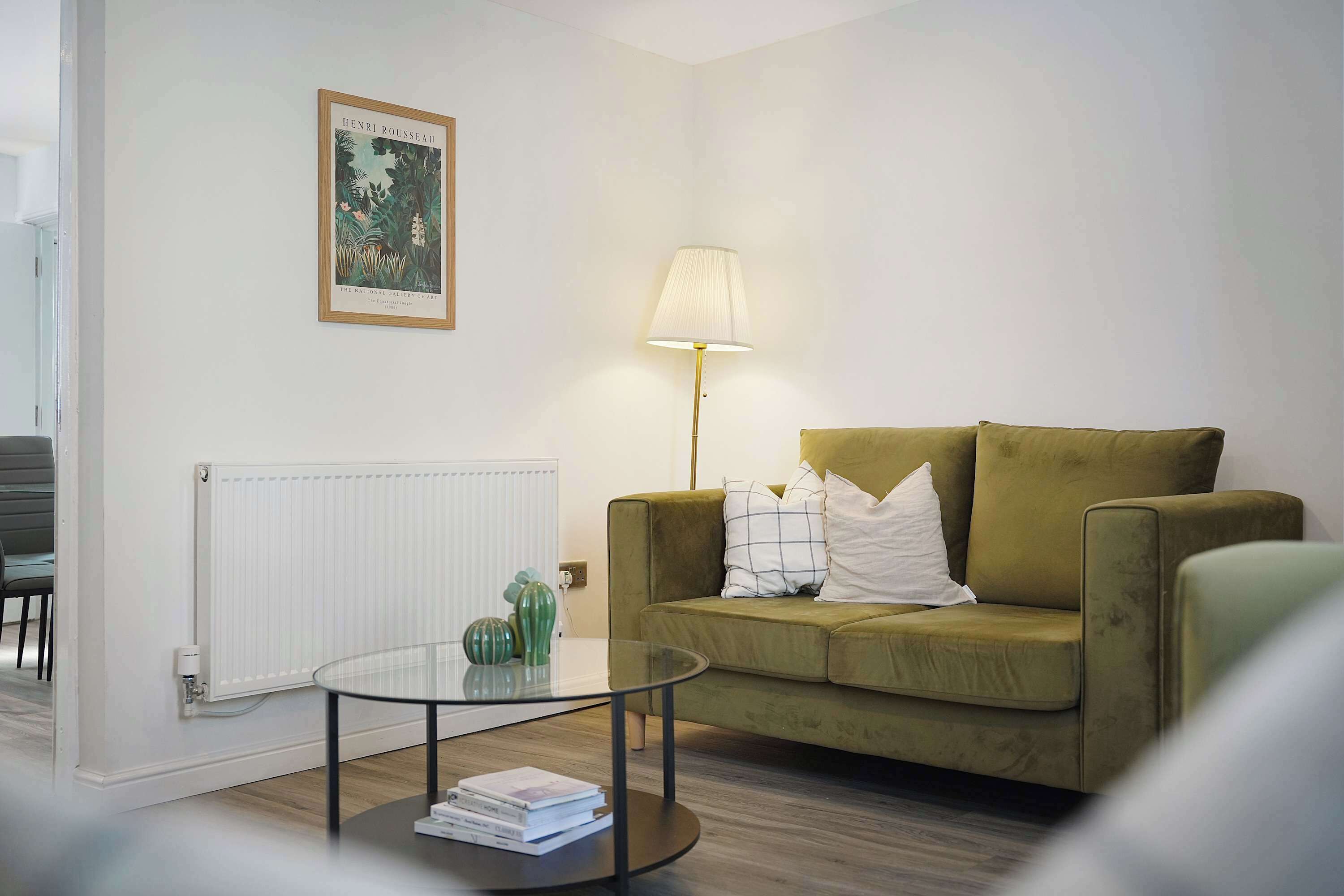 A living room with a green sofa, a glass coffee table, a lamp, and a framed picture on the wall.