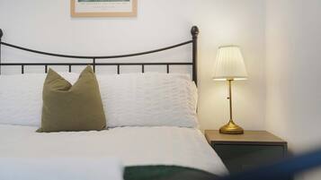 A neatly made bed with white bedding and two pillows, a black metal headboard, a bedside table with a lamp, and a framed picture on the wall.