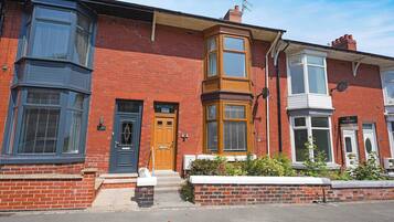 A red brick terraced house with a bay window, a front door, and a small front garden.