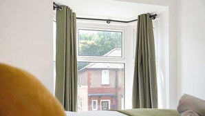 Una habitación con cama, ventana con cortinas y vista a un edificio.
