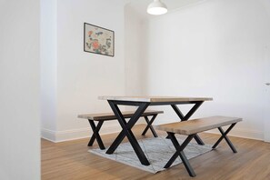 Ein schlichter Raum mit einem Holztisch und einer Bank, einem Teppich und einem gerahmten Bild an der Wand.