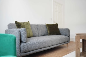 Ein graues Sofa mit zwei Kissen, ein Holztisch und eine weiße Tür in einem Raum mit Holzdielen.