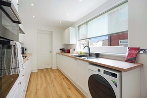 A compact kitchen with a built-in dishwasher, a window with a view of the outside, and a wooden floor. - Comfortable 4BR Stay Byerley Road | Sleeps 7+WiFi (County Durham)