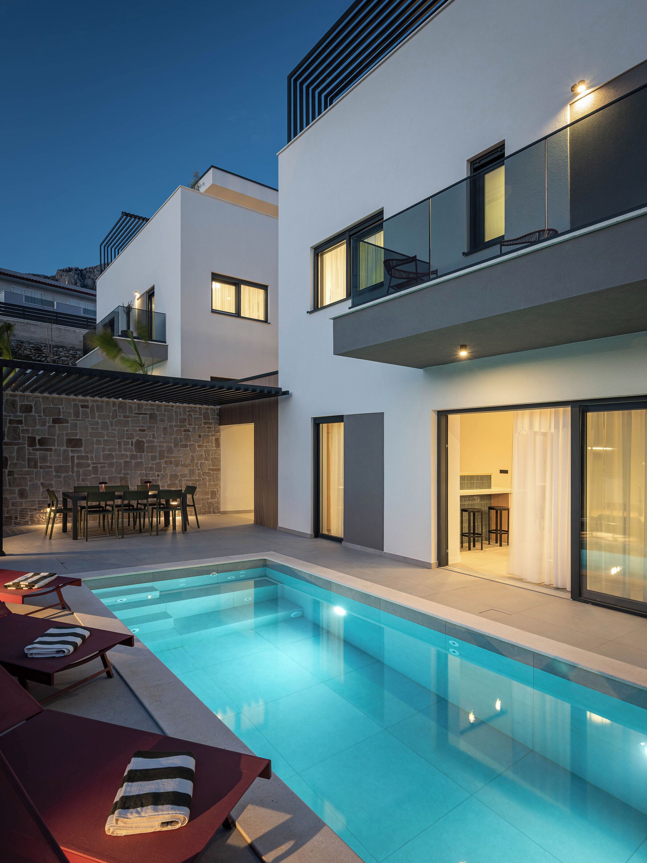 A modern poolside area with a rectangular pool, lounge chairs, and a dining area with tables and chairs.