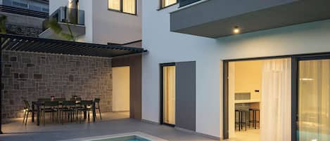 A modern poolside area with a rectangular pool, lounge chairs, and a dining area with tables and chairs.