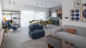 A modern living room with a sofa, armchair, and dining area with chairs. - Villa Respiro Residence South (Kastela)