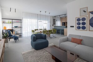 A modern living room with a sofa, armchair, and dining area with chairs. - Villa Respiro Residence South (Kastela)