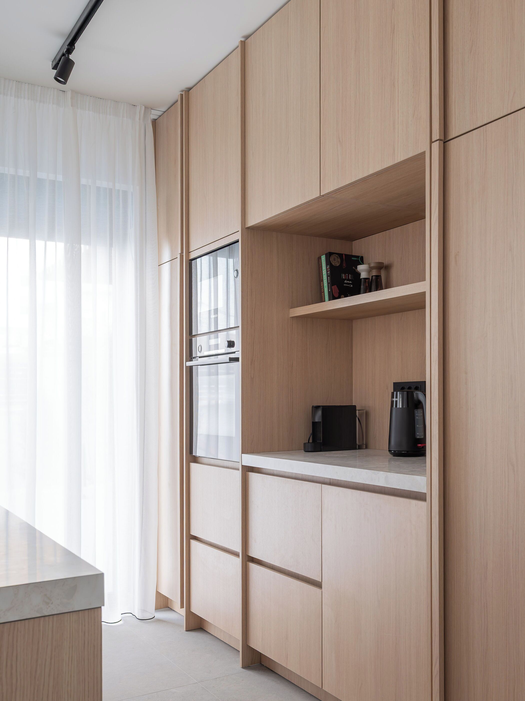 A modern kitchen with wooden cabinetry, a built-in oven, and a coffee maker on the countertop.