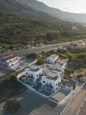 A residential area with modern buildings, a road, and a mountainous backdrop. - Villa Respiro Residence South (Kastela)