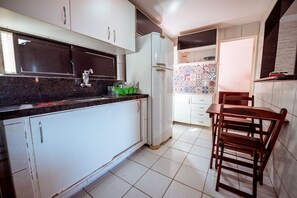 Uma cozinha com armários brancos, geladeira, pia e um espaço de jantar com cadeiras de madeira.