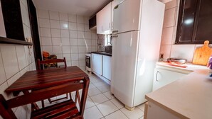 A compact kitchen with a white refrigerator, a wooden table, and a chair. - Apto c 3 Quartos e Garagem a 260 m da Praia (João Pessoa)