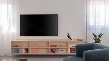 Ein modernes Wohnzimmer mit einem Flachbildfernseher, einer Holz-Unterhaltungsecke, einem blauen Sofa und einem Topf mit Pflanze.