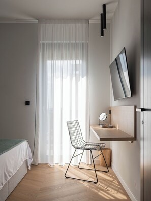 A minimalist bedroom with a bed, a desk with a mirror, a chair, and a TV mounted on the wall. - Villa Respiro Residence North (Kastela)