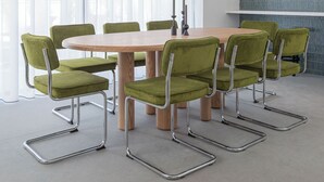Ein moderner Essbereich mit einem runden Tisch, grünen Polsterstühlen, Pendelleuchten und einer Küche im Hintergrund.