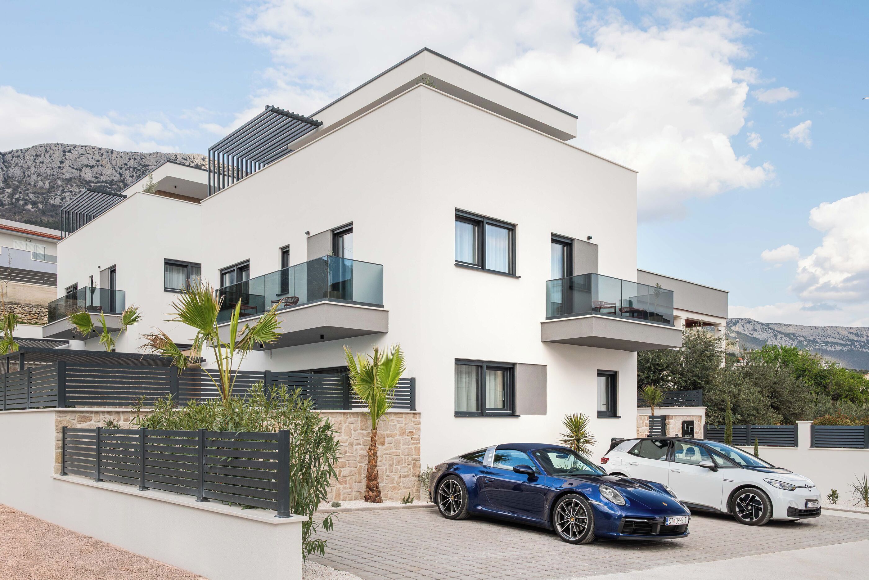 A modern two-story building with balconies, a paved driveway, and two parked cars.