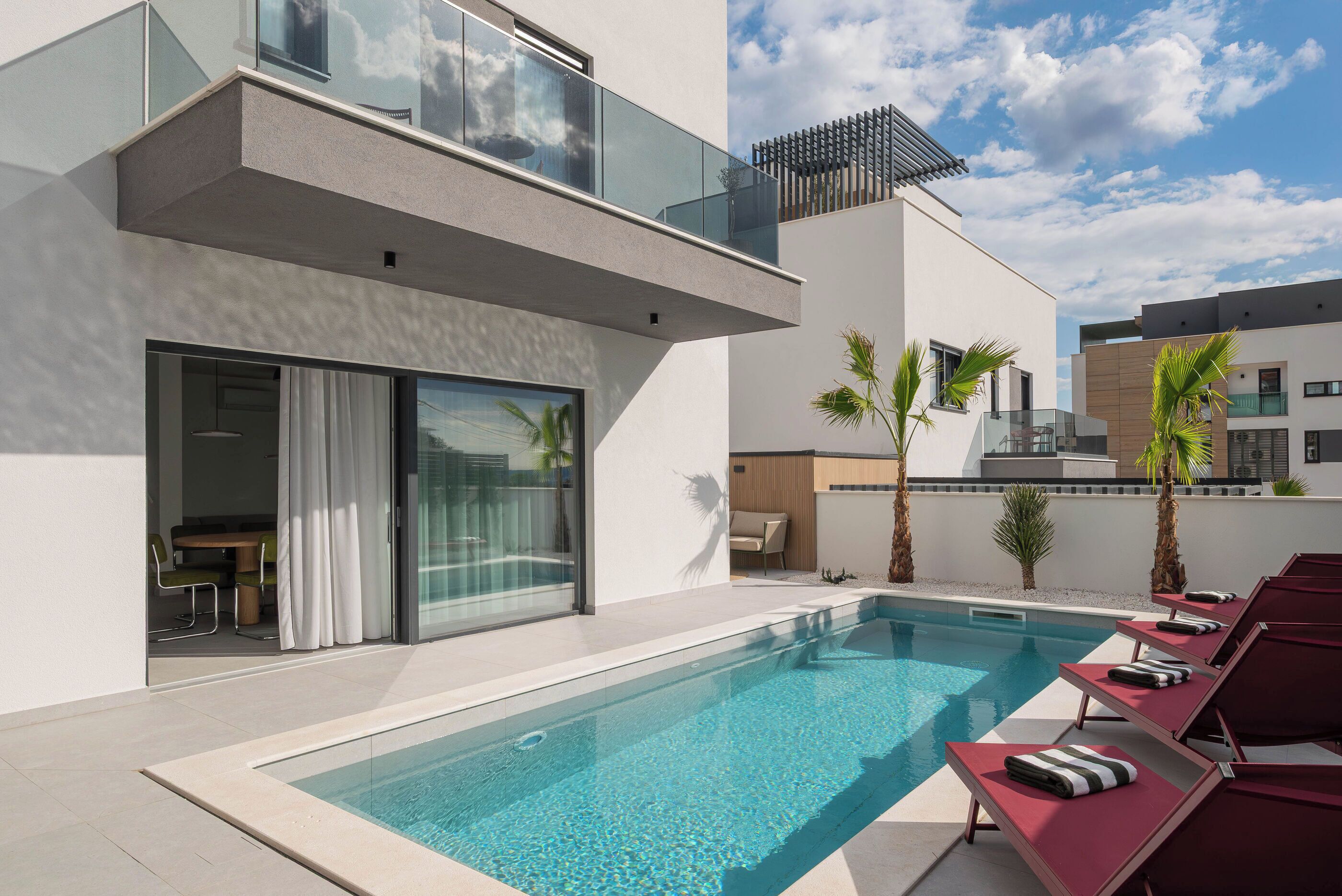 A modern pool area with a clear pool, lounge chairs, and a glass balustrade.