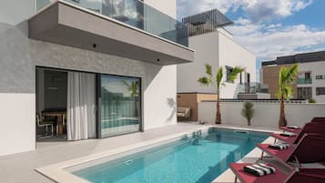 Ein moderner Poolbereich mit klarem Wasser, Liegestühlen und einer Glasbrüstung.