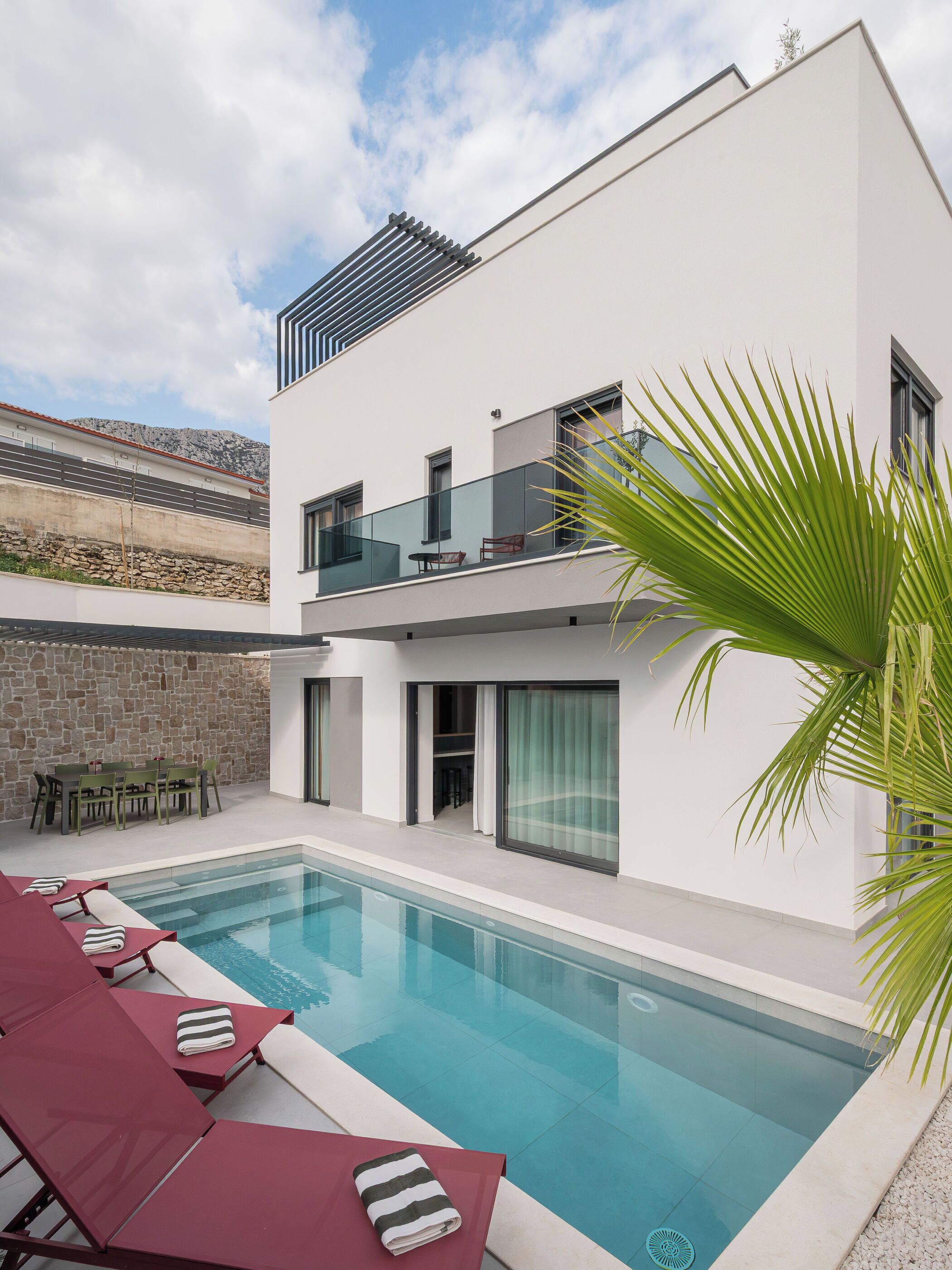 A modern two-story house with a swimming pool, outdoor seating, and a stone wall.