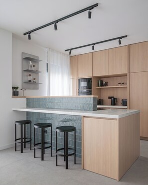 A modern kitchen with a central island, bar stools, wooden cabinets, and built-in appliances. - Villa Respiro Residence North (Kastela)