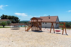 A playground with a wooden swing set and a climbing structure, a swimming pool, and a building with a tiled roof. - Villa Zrilic With Private Pool (Benkovac)