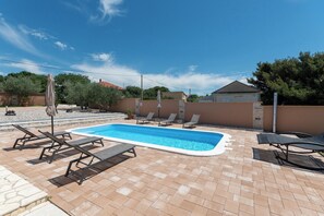 A rectangular swimming pool with lounge chairs and umbrellas, surrounded by a brick patio and a low wall. - Villa Zrilic With Private Pool (Benkovac)