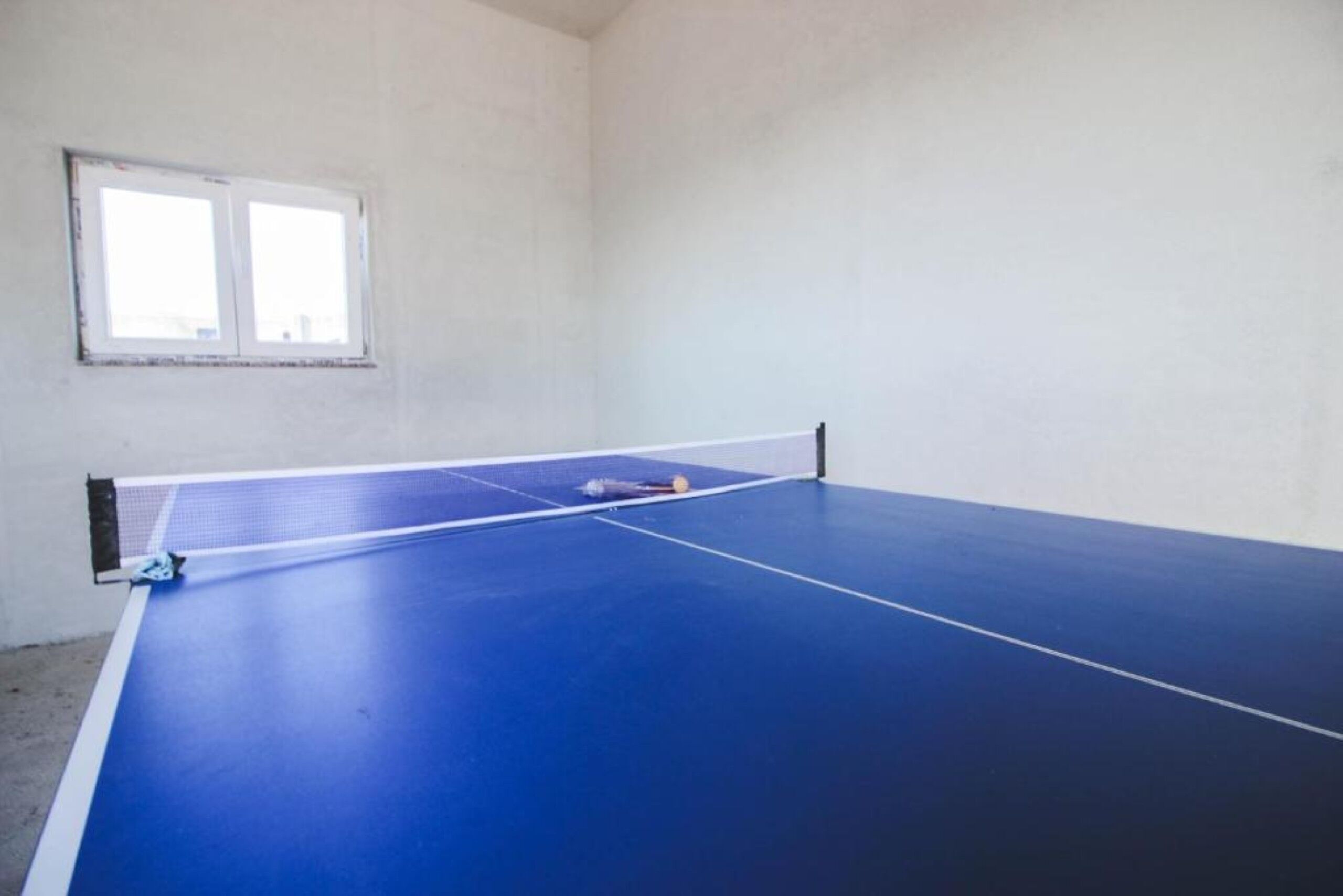Ein Raum mit einem blauen Tischtennis-Tisch, einem Fenster und einer weißen Wand.