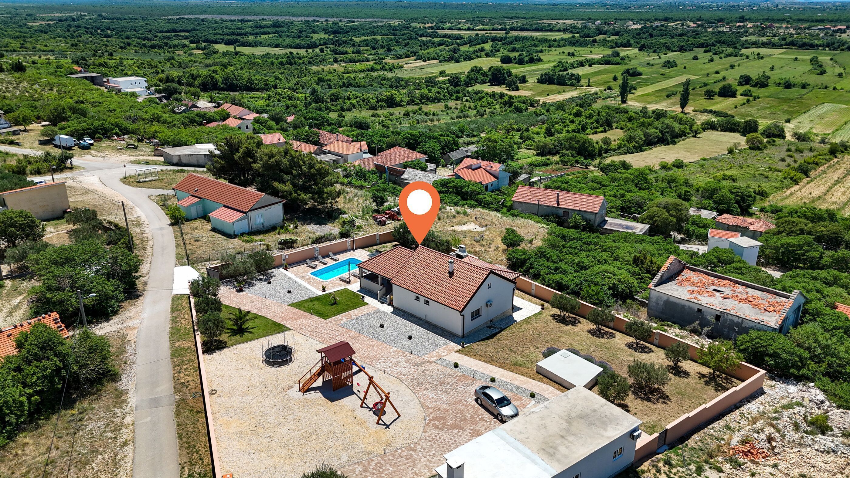 An aerial view of a residential area with houses, a swimming pool, and a playground.