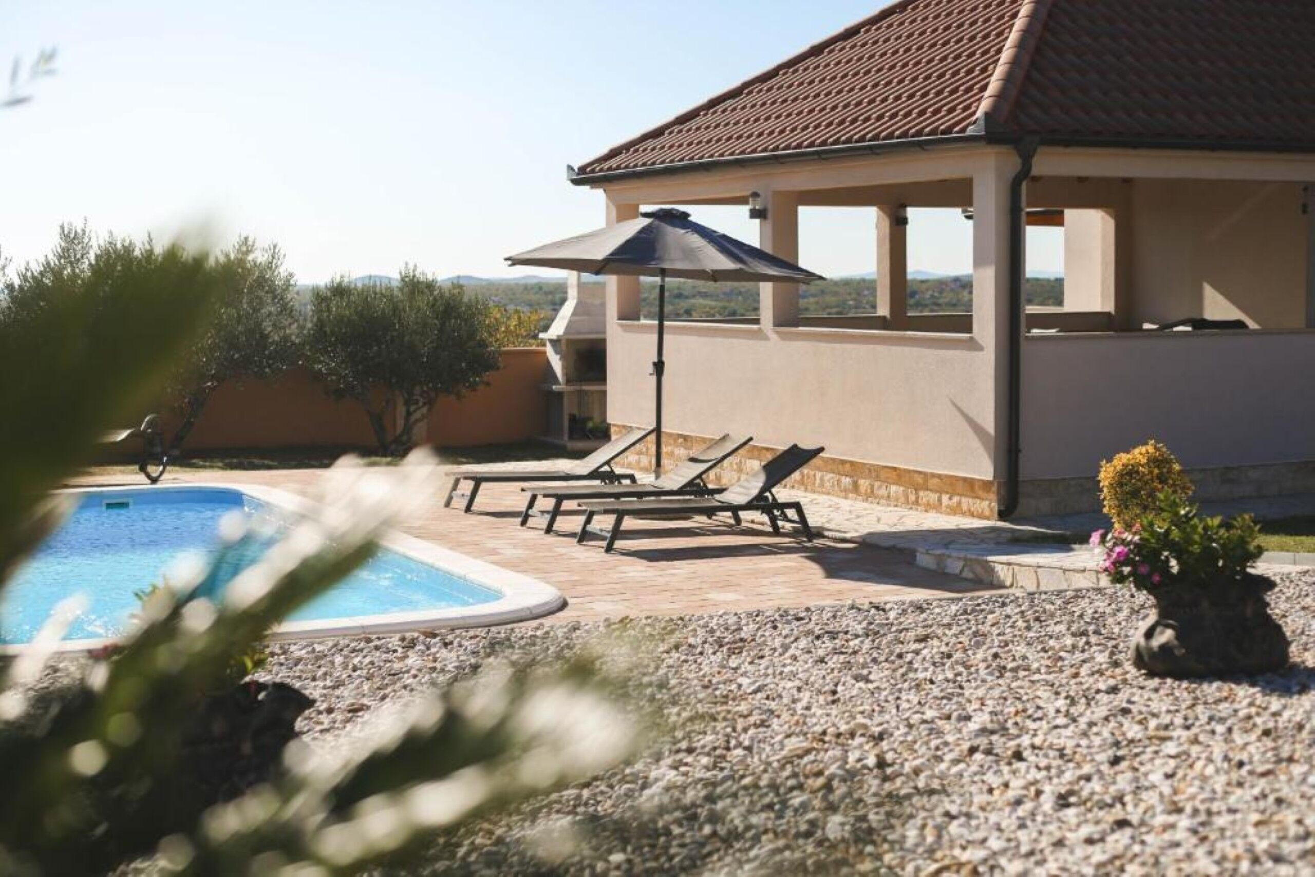 A swimming pool with lounge chairs and an umbrella, surrounded by a pebble-covered patio.