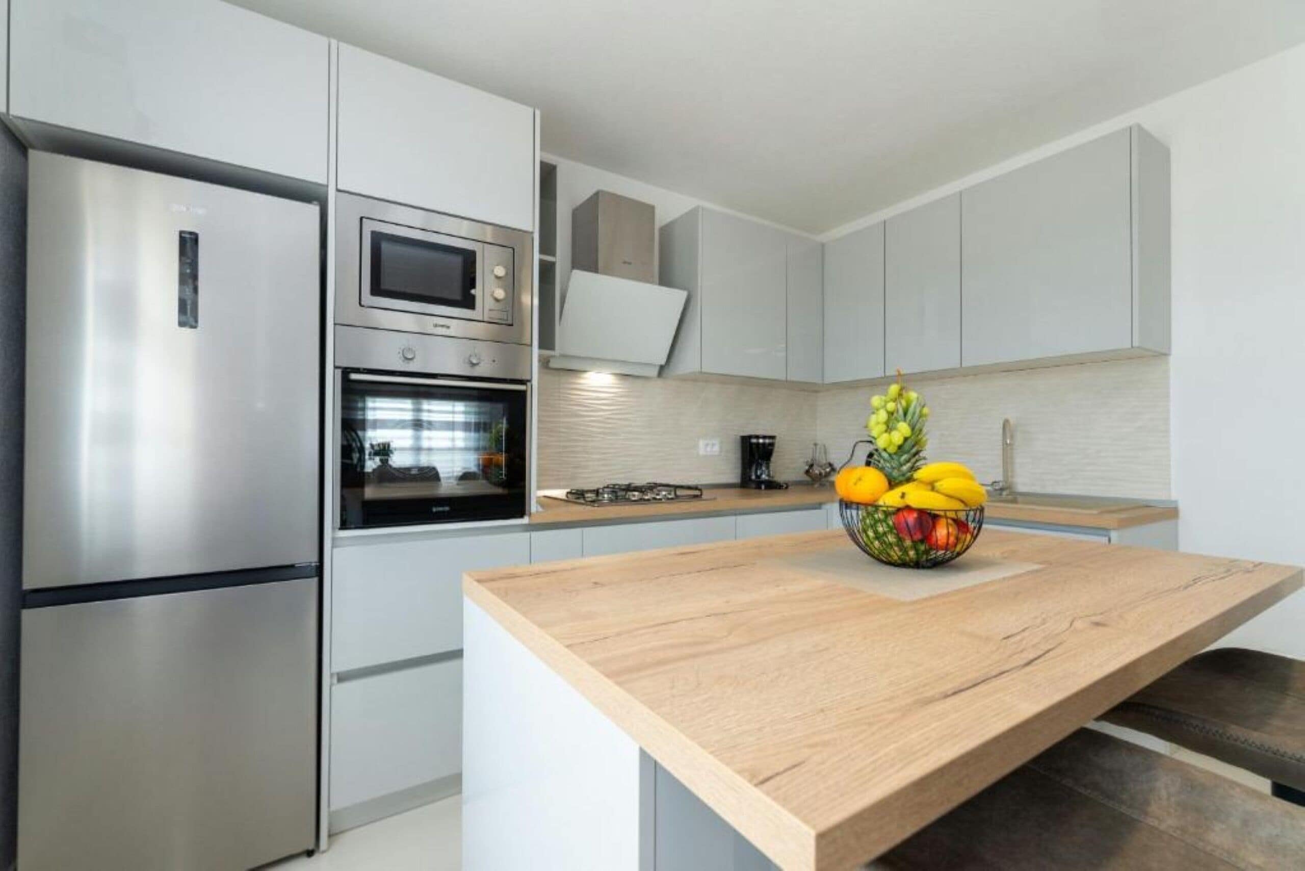A modern kitchen with stainless steel appliances, a wooden countertop, and a fruit bowl.