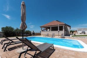 A swimming pool with lounge chairs and an umbrella, a covered patio area, and a clear blue sky. - Villa Zrilic With Private Pool (Benkovac)