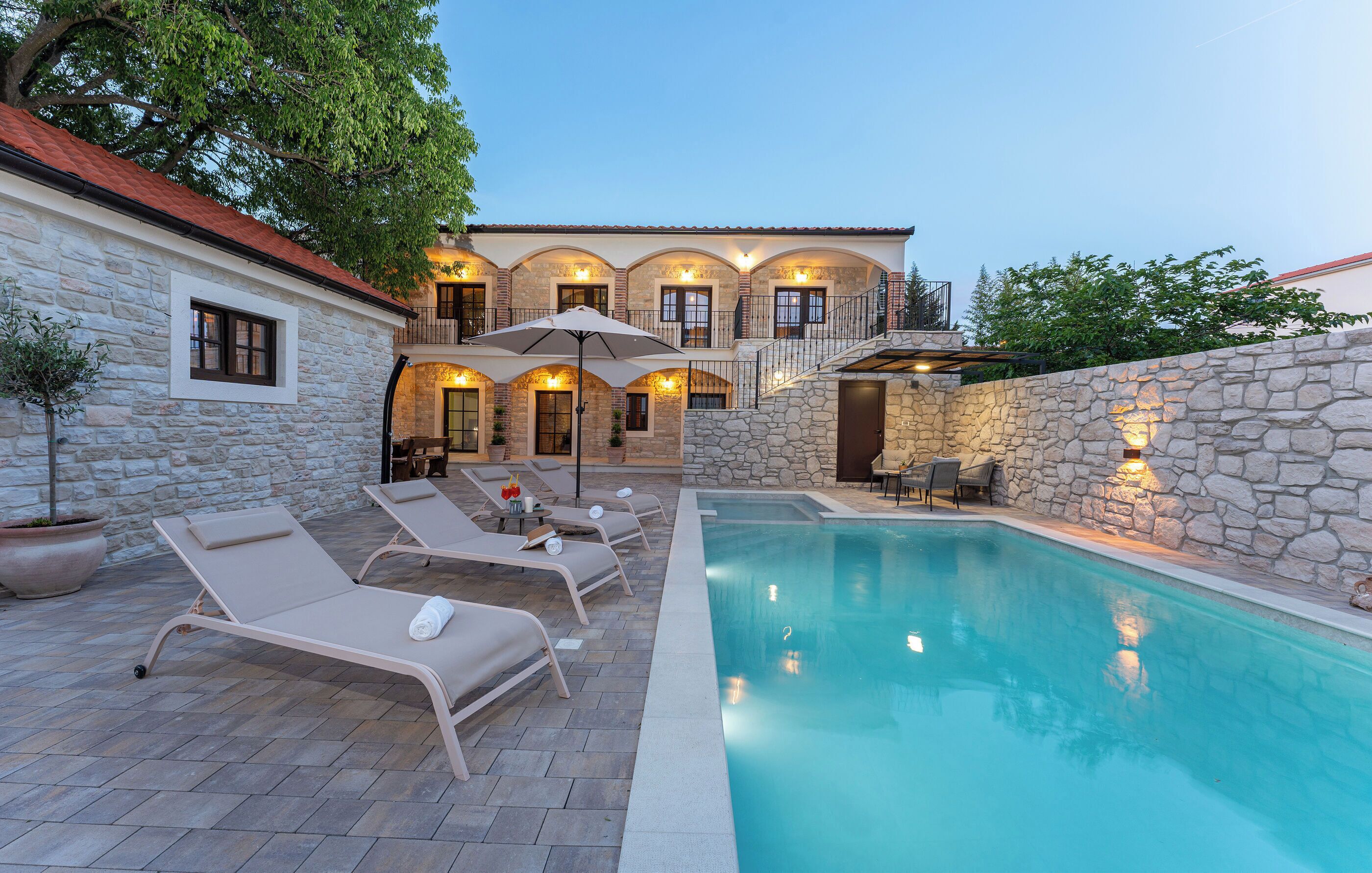 A stone building with a swimming pool, lounge chairs, and outdoor lighting.