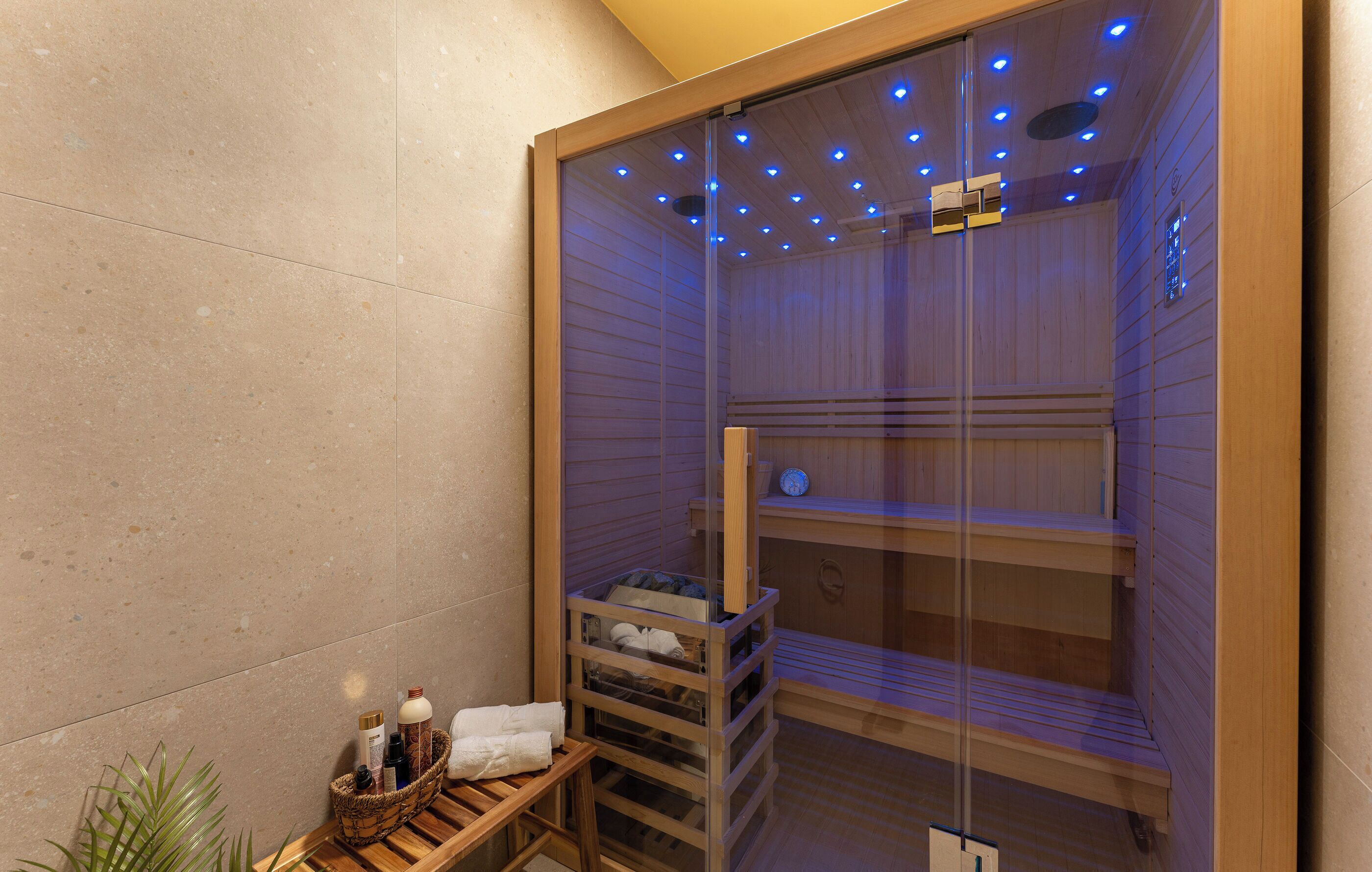 A sauna with glass walls, wooden benches, and a shelf with towels and bottles.