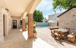 Eine Terrasse mit Steinboden, einem Pool und Gartenmöbeln.